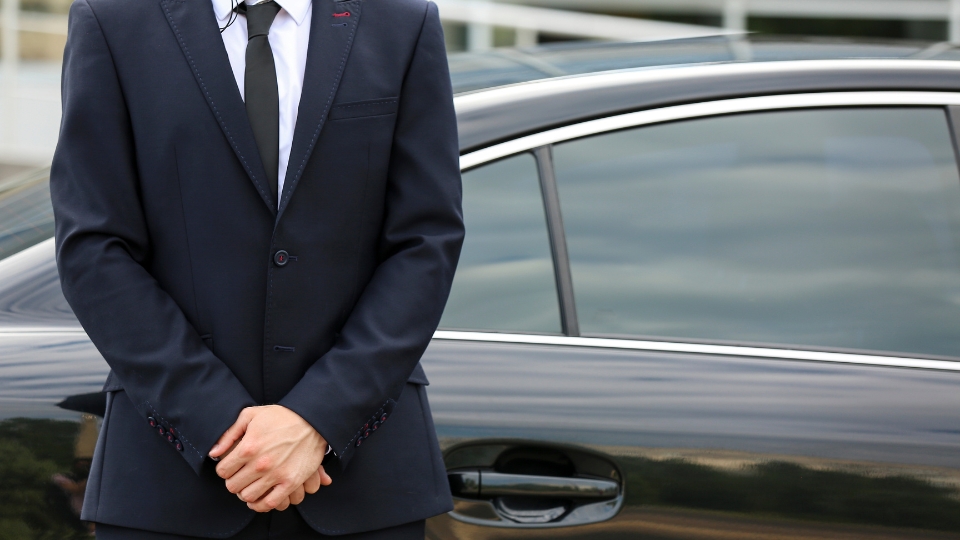 Close-up of a bodyguard in a tailored suit beside a luxury car, illustrating discreet private security and bodyguard services in Brazil.