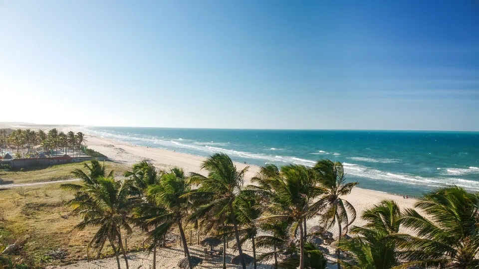 Foto de uma praia paradisíaca no Brasil com mar azul cristalino, areia clara e vegetação tropical ao fundo. Ideal para ilustrar o turismo no Brasil.