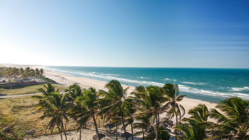 Picture of a paradisiacal beach in Brazil with crystal-clear blue waters, light sand, and lush tropical greenery. Perfect to showcase tourism in Brazil.