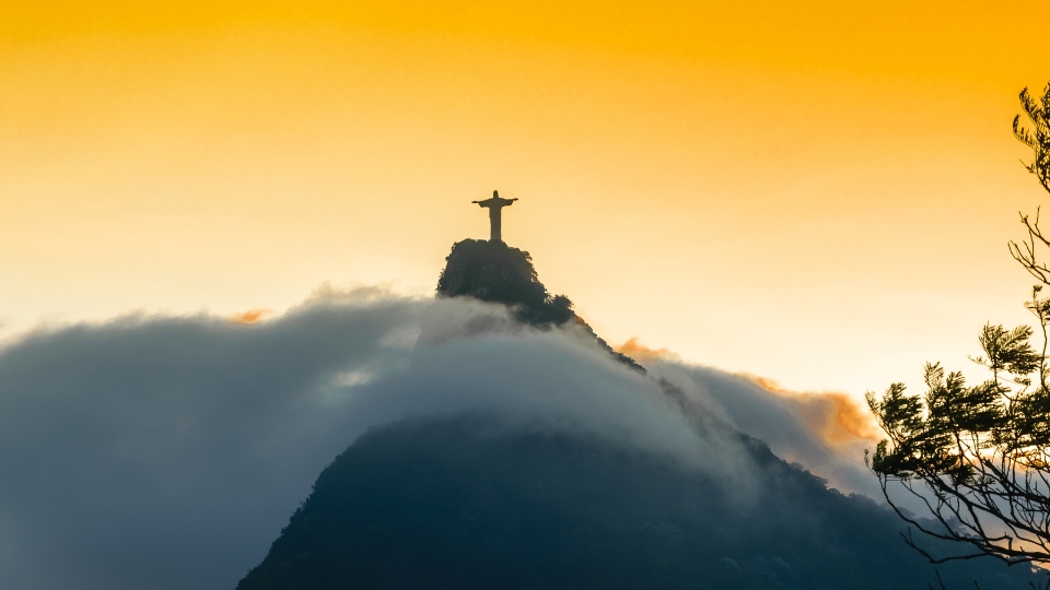 Christ the Redeemer overlooking Rio de Janeiro at sunset, with the city and coastline illuminated below