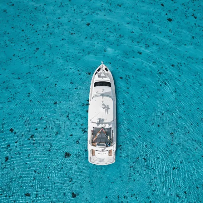pexels-photo-10680487-10680487 Top-down view of a white yacht in clear turquoise waters, surrounded by ripples.