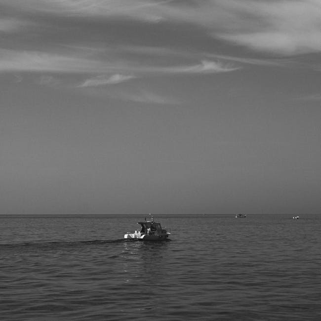pexels-photo-18846182-18846182 A serene black and white image of a motorboat gliding over the ocean under a cloudy sky.