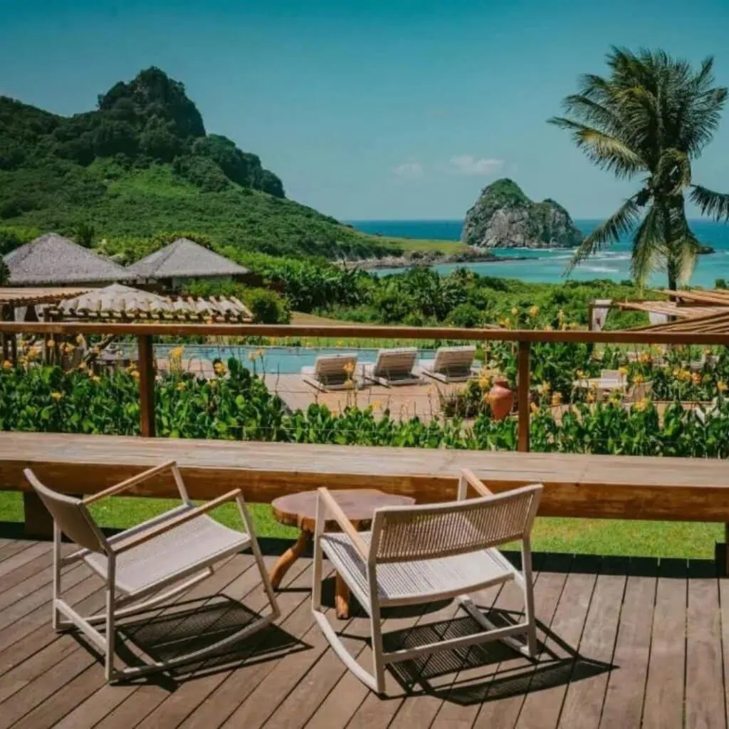 Seaside terrace with chairs overlooking lush green hills and ocean in Brazil.