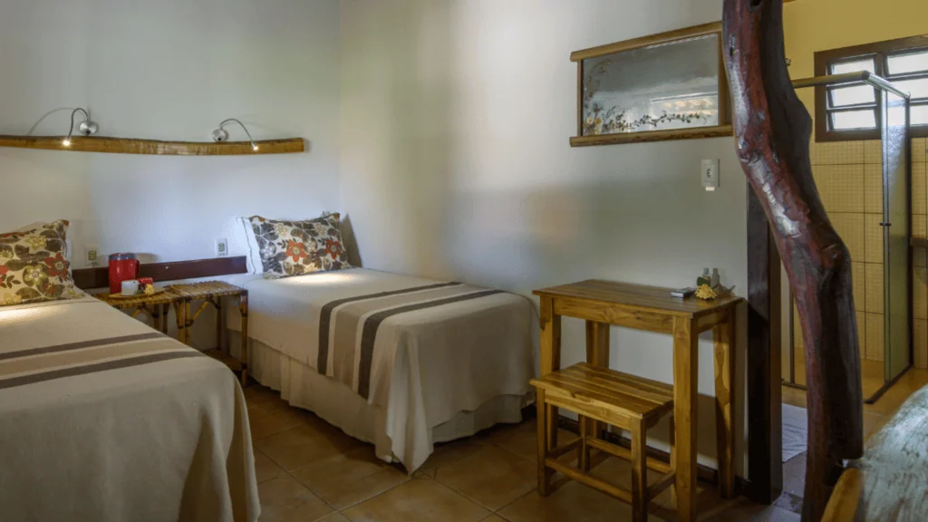 Araras Ecolodge - Hotel Booking in the pantanal (6) Interior of a bedroom at Araras Ecolodge with two beds, wooden furniture, and a shower area visible.