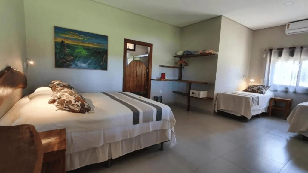 Araras Ecolodge - Hotel Booking in the pantanal (8) Interior of a bedroom at Araras Ecolodge with two beds, a painting, and a window with curtains.