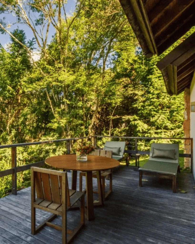 Balcony with wooden table, chairs, and lush green trees in the background at Botanique Hotel.