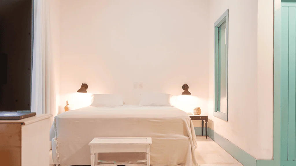 Casa Brasileira Hotel - Hotel Booking in the northeast (11) Bedroom with white bed, two wall-mounted lamps, and a window in Casa Brasileira.