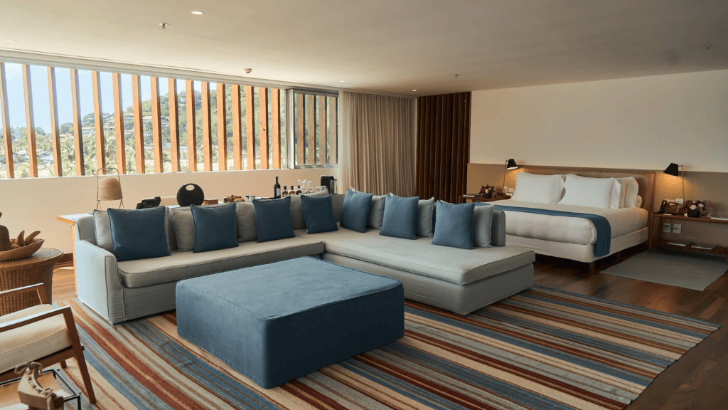 Fasano Angra dos Reis - Hotel Booking in Angra dos Reis (7) Spacious hotel suite with large window, modern sofa, and king-size bed in the Fasano hotel.
