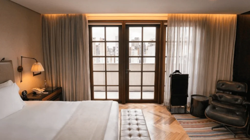 Fasano São Paulo - Hotel Booking in Sao Paulo (5) Hotel room with large window overlooking city skyline, modern decor, and leather armchair.