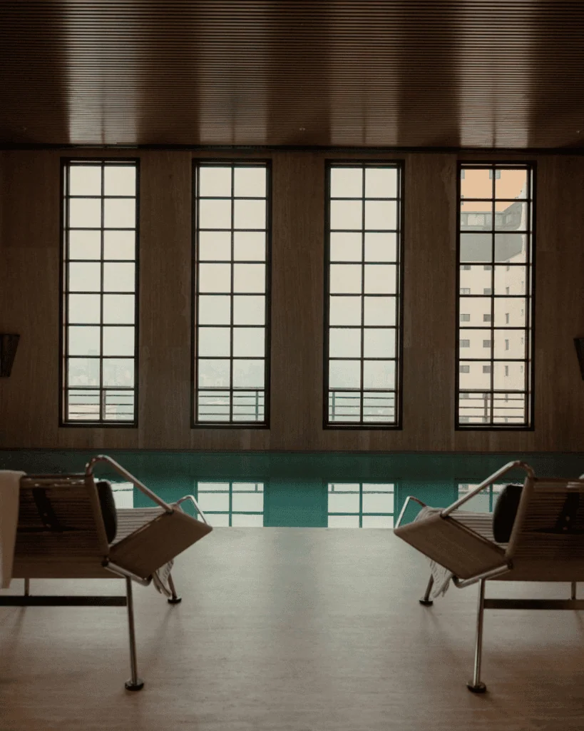 Indoor pool area with large windows and two lounge chairs facing the pool.