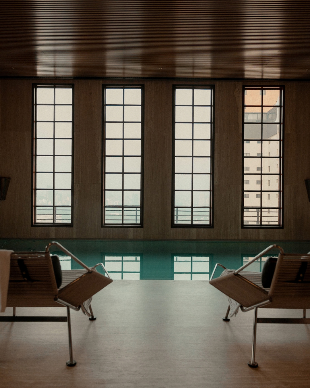 Indoor pool area with large windows and two lounge chairs facing the pool.