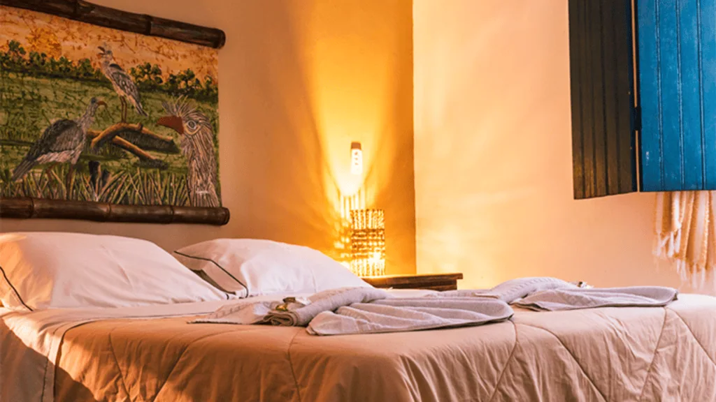 Pousada Aguapé - Hotel Booking in the pantanal (6) Interior of a bedroom at Pousada Aguapé with a bed, wall art, and warm lighting.