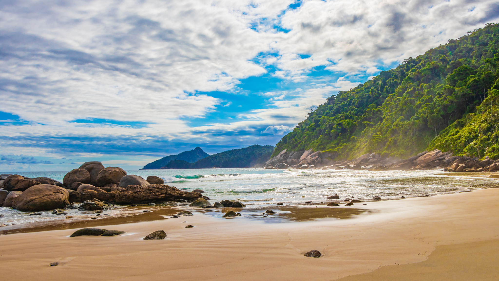 Beach with rocks, green hills, and cloudy sky near Paraty, Brazil.